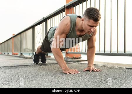 L'homme musclé fait des push-ups pendant l'entraînement calisthénique dans une rue Banque D'Images