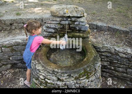 Adorable petite fille remplissant une bouteille d'eau dans une fontaine en pierre dans un bois. Vacances en Italie Banque D'Images