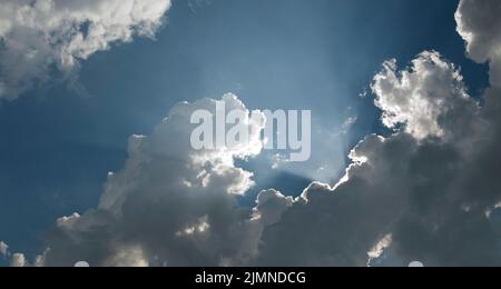 les rayons du soleil se brisent derrière les nuages gris avec le ciel bleu Banque D'Images