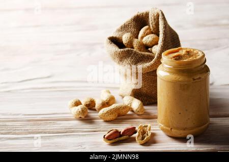 Vue en bas angle sur le pot de maçon en verre avec beurre d'arachide sur une table en bois blanc avec sac de toile à dos. Concept de saine alimentation Banque D'Images