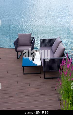 Canapés confortables et table sur une terrasse en bois au bord de l'eau. Un bel endroit pour se détendre sur l'étang. Espace de loisirs et de détente. Banque D'Images