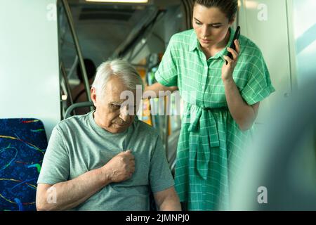 Femme appelant à la ligne d'urgence parce que l'homme âgé a des symptômes de crise cardiaque dans les transports publics Banque D'Images