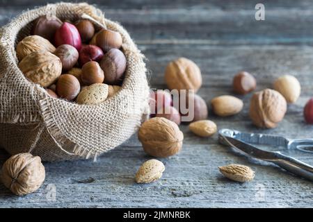 Des noix entières dans un sac de toile de jute avec un peu déversées sur une table rustique. Banque D'Images