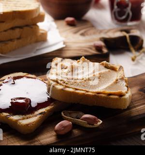 Vue à bas angle sur le beurre d'arachide et les sandwichs de confiture à bord de la planche à découper avec toasts de côté. Concept de saine alimentation Banque D'Images