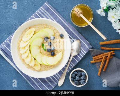 Flocons d'avoine avec bananes, bleuets, confiture, miel, serviette bleue sur fond de pierre bleue. Banque D'Images