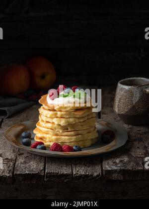 Crêpe à la crème vanille, aux myrtilles et aux framboises. Vue latérale, verticale, espace de copie. Arrière-groun en bois rustique sombre et sombre Banque D'Images