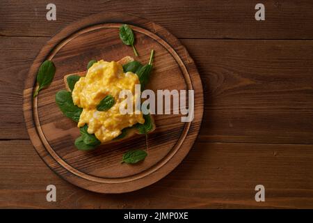 Toast aux œufs brouillés et aux épinards. Omelette. Petit déjeuner avec œufs poêlés sur fond brun foncé. Vue de dessus. Banque D'Images