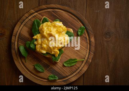 Toast aux œufs brouillés et aux épinards. Omelette. Petit déjeuner avec œufs poêlés sur fond brun foncé. Vue de dessus. Banque D'Images