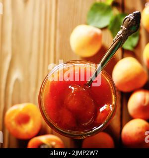 Pot en verre de confiture d'abricot sur table en bois avec des abricots mûrs à l'arrière-plan. Vue d'en haut. Banque D'Images