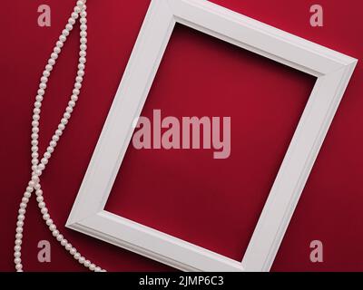 Cadre d'art vertical blanc et bijoux en perles sur fond rouge comme motif de placolatte, imprimé d'art ou album photo Banque D'Images