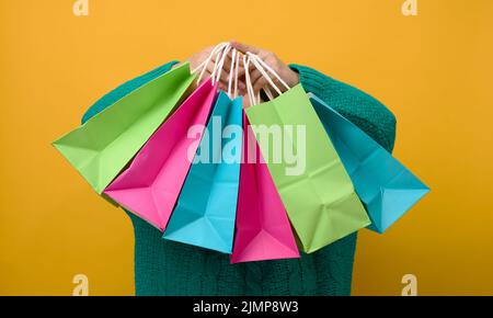 Une femme dans un chandail tient un sac en papier sur un fond jaune et montre un geste semblable avec sa main. Achats. Solde saisonnier Banque D'Images