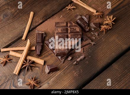 Morceaux de chocolat noir cassés, bâtonnets de cannelle et anis étoilé sur une table en bois marron, vue du dessus Banque D'Images
