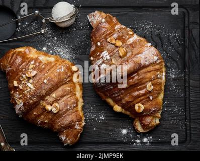 Croissant cuit sur une planche de bois et arrosé de sucre en poudre, table noire. Pâtisseries appétissantes pour le petit déjeuner Banque D'Images