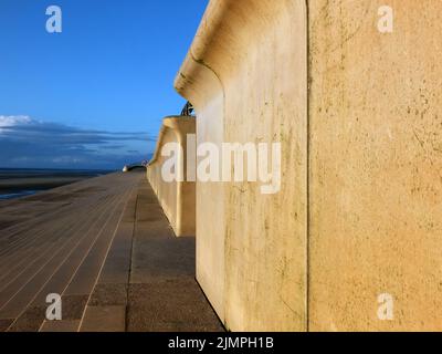 Vue en perspective sur le sentier côtier en béton de blackpool avec des marches menant à la plage dans la lumière chaude de l'après-midi avec du bleu Banque D'Images