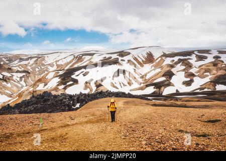 Vue majestueuse depuis le sentier de Brennisteinsalda avec randonnée femelle sur la montagne volcanique et la neige couverte à Landmannalaugar dans les hauts plateaux de l'Islande Banque D'Images