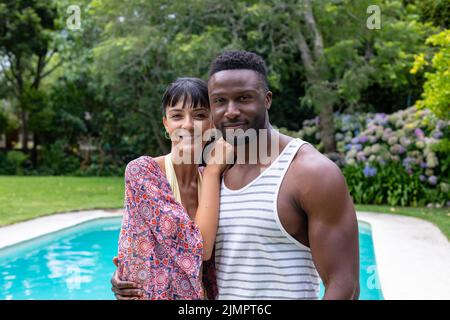 Portrait de jeune couple multiracial debout près de la piscine dans l'arrière-cour Banque D'Images