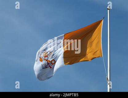 Drapeau de l'État du Vatican volant contre un ciel bleu clair éclairé par le soleil Banque D'Images