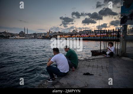 Istanbul, Turquie. 06th août 2022. Les gens ont vu assis sur la côte de Karaköy et le pont historique de Galata en arrière-plan pendant la soirée à Istanbul. Crédit : SOPA Images Limited/Alamy Live News Banque D'Images