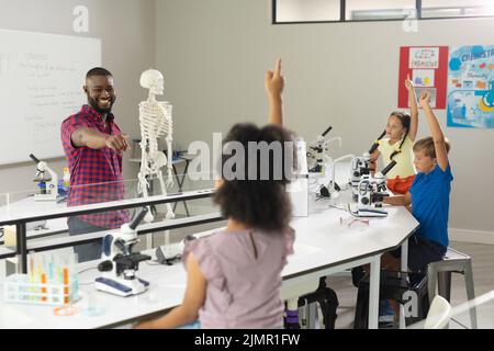 Souriant, un jeune enseignant afro-américain se dirige vers une jeune fille de l'école élémentaire biraciale en laboratoire Banque D'Images