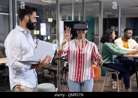 Femme d'affaires biraciale portant un casque vr par un homme d'affaires caucasien avec un ordinateur portable pendant la réunion Banque D'Images