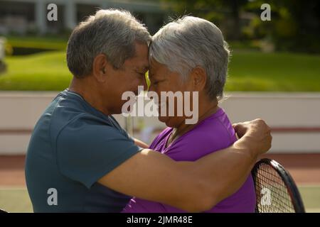 Gros plan d'un couple biracial heureux avec les yeux fermés et le romantisme face à face sur le court de tennis Banque D'Images