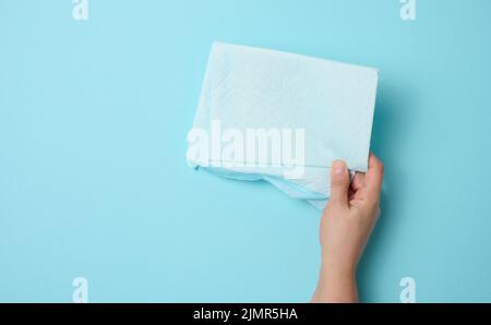 La main femelle tient une couche médicale jetable sur fond bleu. Produit d'hygiène Banque D'Images