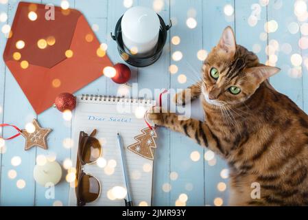 Une lettre au Père Noël, une enveloppe, des jouets de Noël et un chat sur une table en bois. Banque D'Images