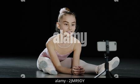 Fille adolescent ballerina acrobat gymnast s'assoit sur le sol regardant la webcam a cours en ligne de danse avec l'entraîneur d'Internet regardant dans Banque D'Images