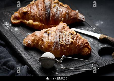 Croissant cuit sur une planche de bois et arrosé de sucre en poudre, table noire. Pâtisseries appétissantes pour le petit déjeuner Banque D'Images