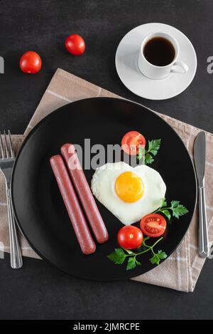 Œufs brouillés avec saucisse et légumes servis sur une assiette sur fond sombre. Banque D'Images