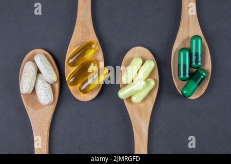 Petites cuillères en bois avec suppléments, vitamines et pilules en bois brun clair sur fond sombre, vue de dessus. Banque D'Images