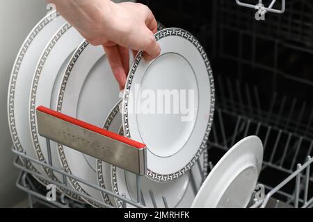 La main femelle sort une plaque propre du lave-vaisselle. Nettoyez la vaisselle dans le lave-vaisselle en gros plan. Vue de dessus. Banque D'Images