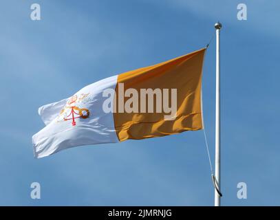 Drapeau de l'État du Vatican volant contre un ciel bleu clair éclairé par le soleil Banque D'Images