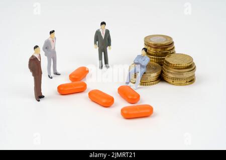 Une figurine miniature d'un homme est assise sur des pièces de monnaie, à côté de lui sont des pilules et des figurines de personnes. Concept d'entreprise médicale Banque D'Images