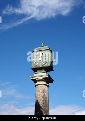 Vieille horloge extérieure en métal vert sur un pilier en pierre dans l'arnside cumbria contre un ciel bleu nuageux Banque D'Images
