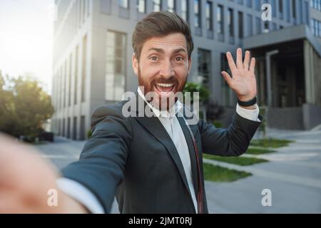 Homme d'affaires heureux en costume faire un selfie sur fond de son immeuble de bureau Banque D'Images