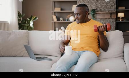 Masculin afro-américain sportif à la retraite faisant biceps boucles pompant des muscles avec des haltères lever des poids pratiquant avec le culturisme en ligne Banque D'Images