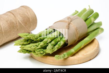 Un bouquet d'asperges fraîches enveloppées de papier brun se trouve dans une assiette en bois Banque D'Images