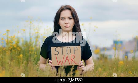 Triste caucasien brunette femme patriote augmenter la plaque avec l'inscription STOP guerre malheureux dépression fille stand seul dehors dans le champ montrer carton Banque D'Images