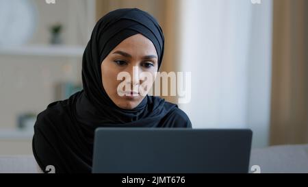 Ciblée ethnique musulmane arabe jeune femme fille islamique étudiante femme d'affaires pigiste assis à la maison travail sur ordinateur en ligne recherche de chat Banque D'Images