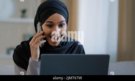 Joyeux sourire femme arabe musulmane fille dans hijab femme freelancer parlant par téléphone mobile avec un ami répondant à l'appel apprécier bonne nouvelle a des affaires Banque D'Images