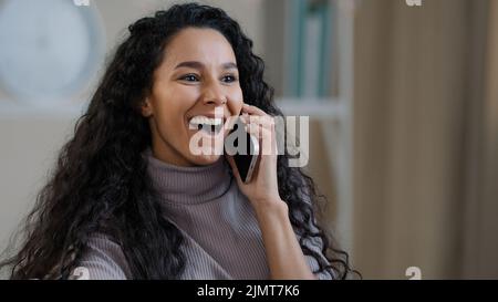 Jolie fille arabe souriante jeune femme parle par téléphone mobile profiter de la conversation sans fil dire des commérages choqué joyeuse heureuse femme millénaire heureuse d'entendre Banque D'Images