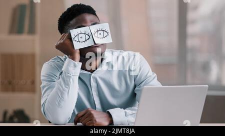 Somnolent drôle african american Office Manager homme d'affaires assis à la maison de travail avec des notes collantes sur les yeux comic jeune travailleur fatigué a sommeil pr Banque D'Images