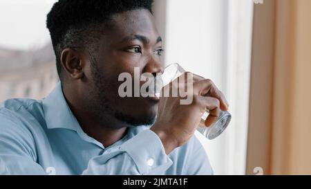 Afro-américain jeune homme rêvant positif réfléchi gars tourner la tête regarder la fenêtre boire eau froide verre d'hydrate liquide pur souffrir de soif Banque D'Images