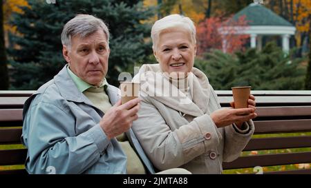 Grand-parents âgés insouciants boire du café chaud thé en plein air senior couple âgé homme femme retraités grand-parents famille s'asseoir sur le banc profiter Banque D'Images