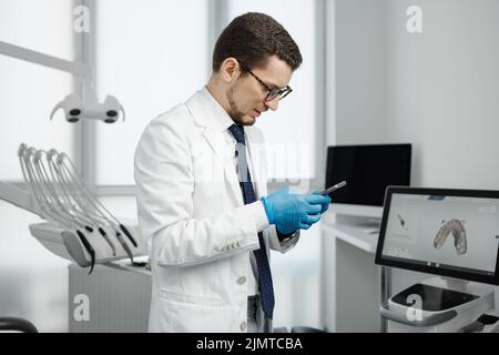 Dentiste masculin élégant utilisant un smartphone dans un cabinet dentaire Banque D'Images