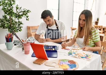 Deux élèves ayant un cours de peinture en ligne utilisant le pavé tactile assis sur la table à l'école d'art. Banque D'Images