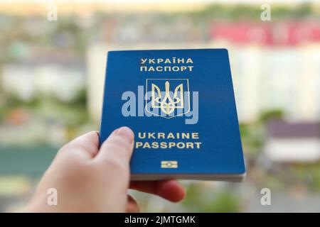 Recentrer le passeport d'un citoyen ukrainien dans une main féminine sur un fond urbain flou, gros plan. Inscription au passeport ukrainien. Guerre. Sortie Banque D'Images