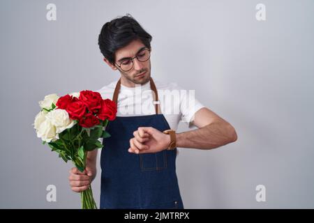 Jeune homme hispanique tenant un bouquet de roses blanches et rouges vérifiant le temps sur la montre de poignet, détendu et confiant Banque D'Images