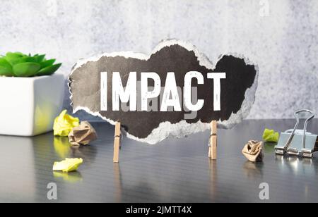 mot d'impact écrit sur fond gris avec des crayons et des trombones. Banque D'Images